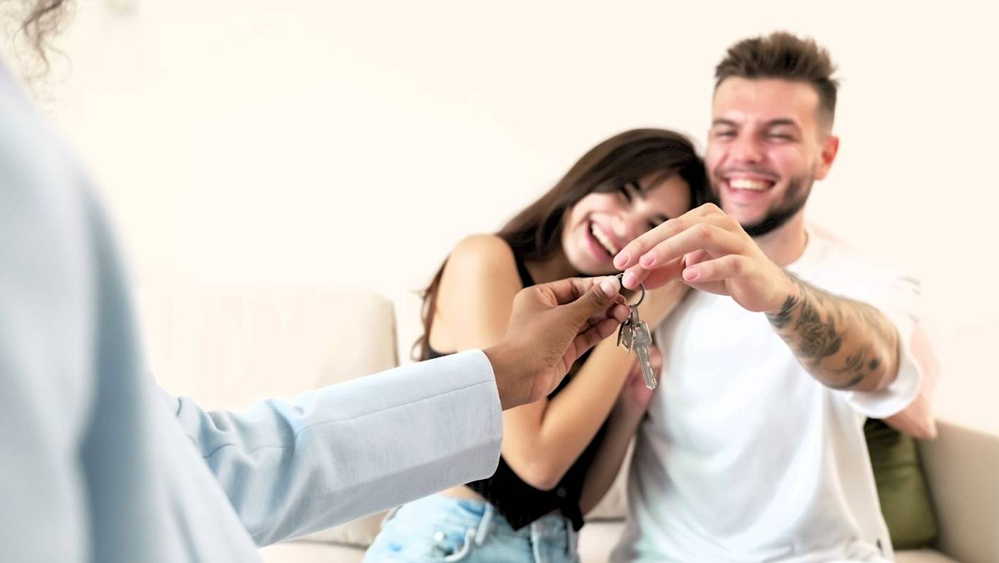 Young male couple sat in front of a laptop and smiling at the screen