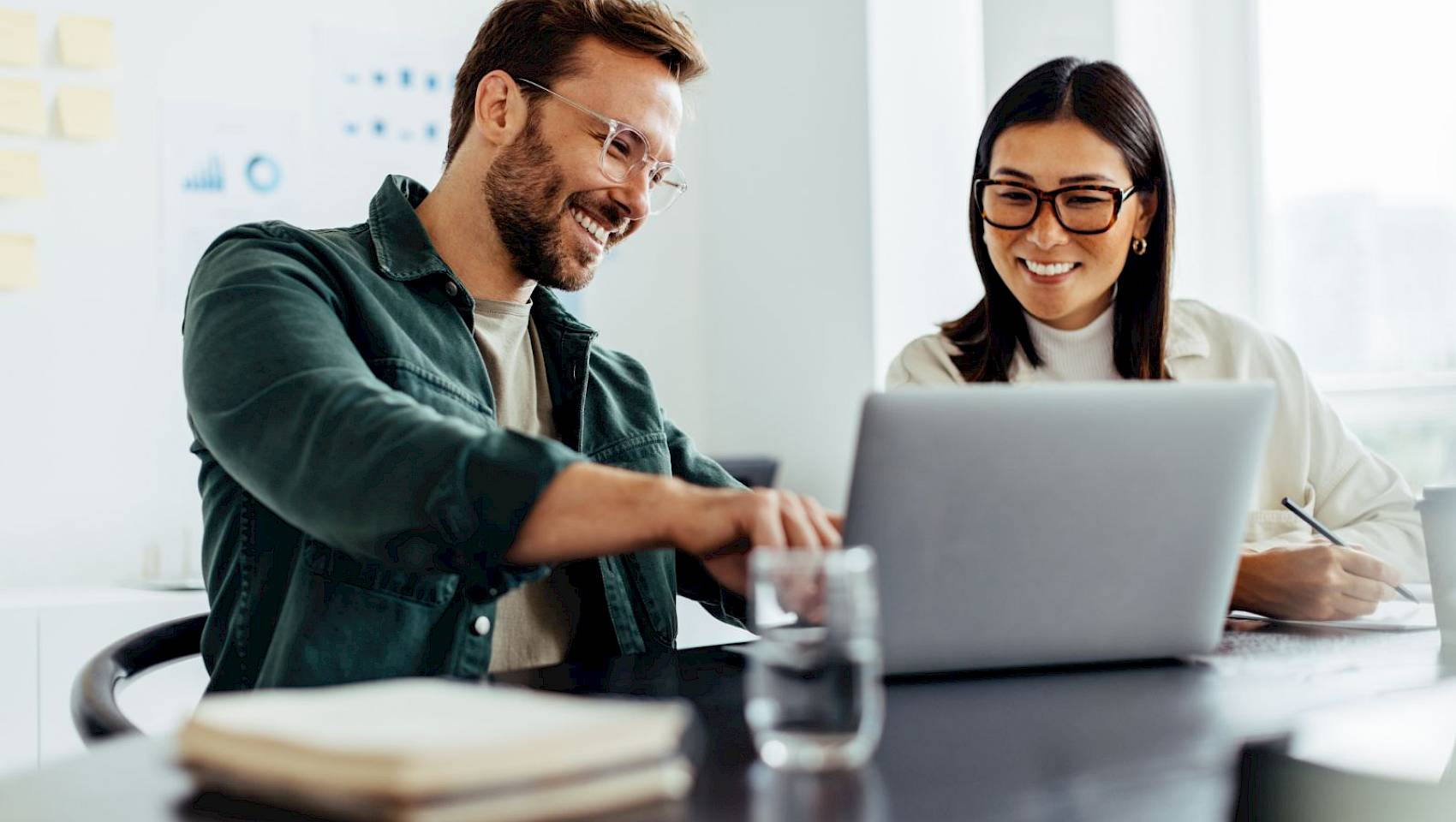 prfoessional male and female looking at laptop screen smiling in office setting